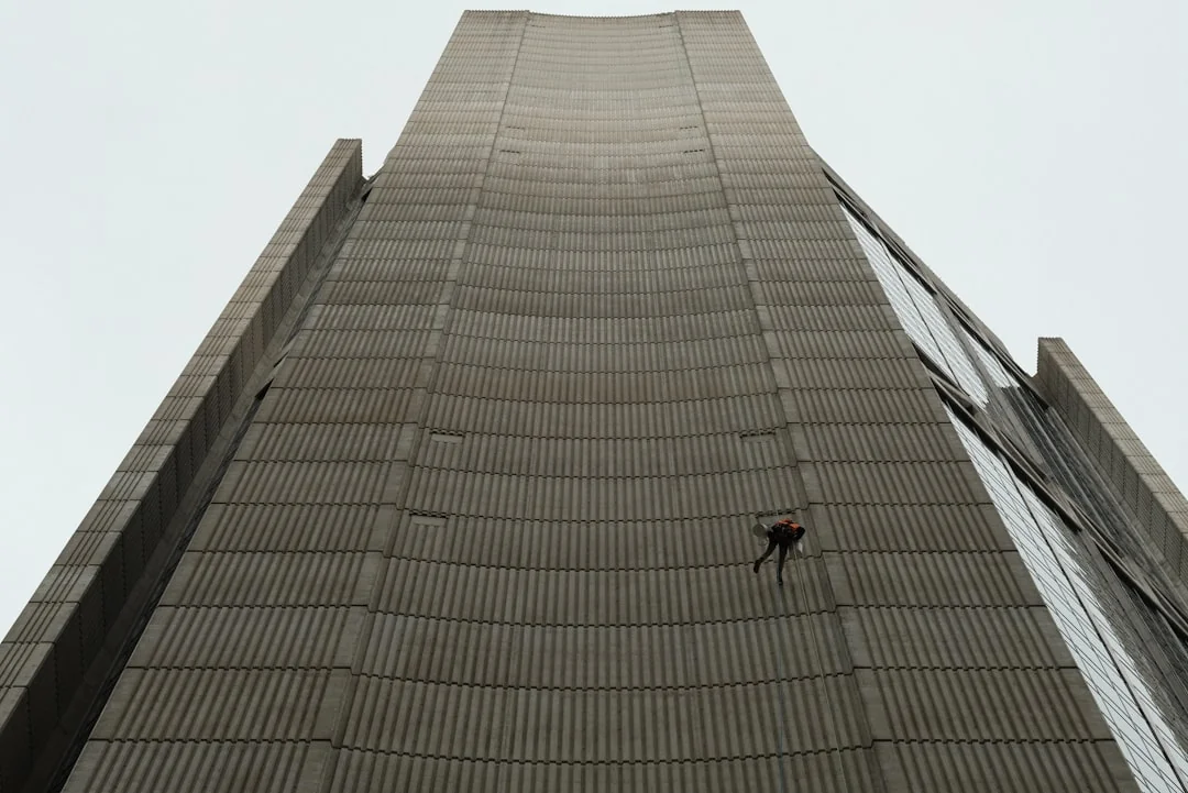 services-03 A man cleaning skyscraper windows with a harness, showcasing urban high-rise work.